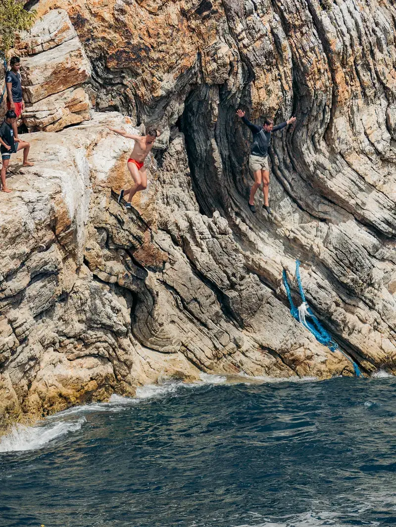 Traveller mid-air leaping off a Coron cliff into turquoise water