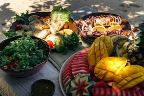 Fresh grilled seafood, salad, and tropical fruit served on a shaded island lunch table during a Seatours speedboat day tour in El Nido